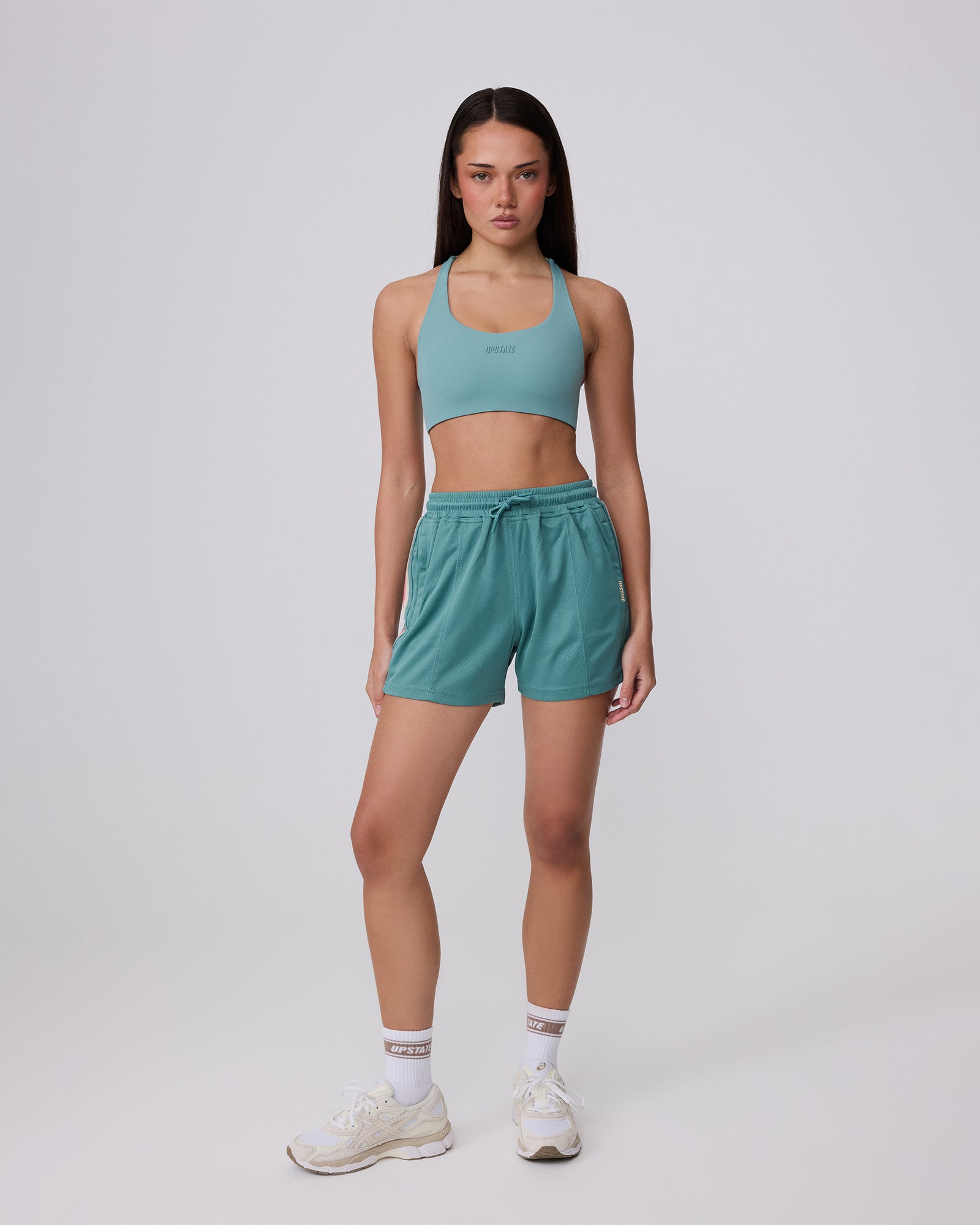 Woman wearing a teal sports bra and shorts set on a white background
