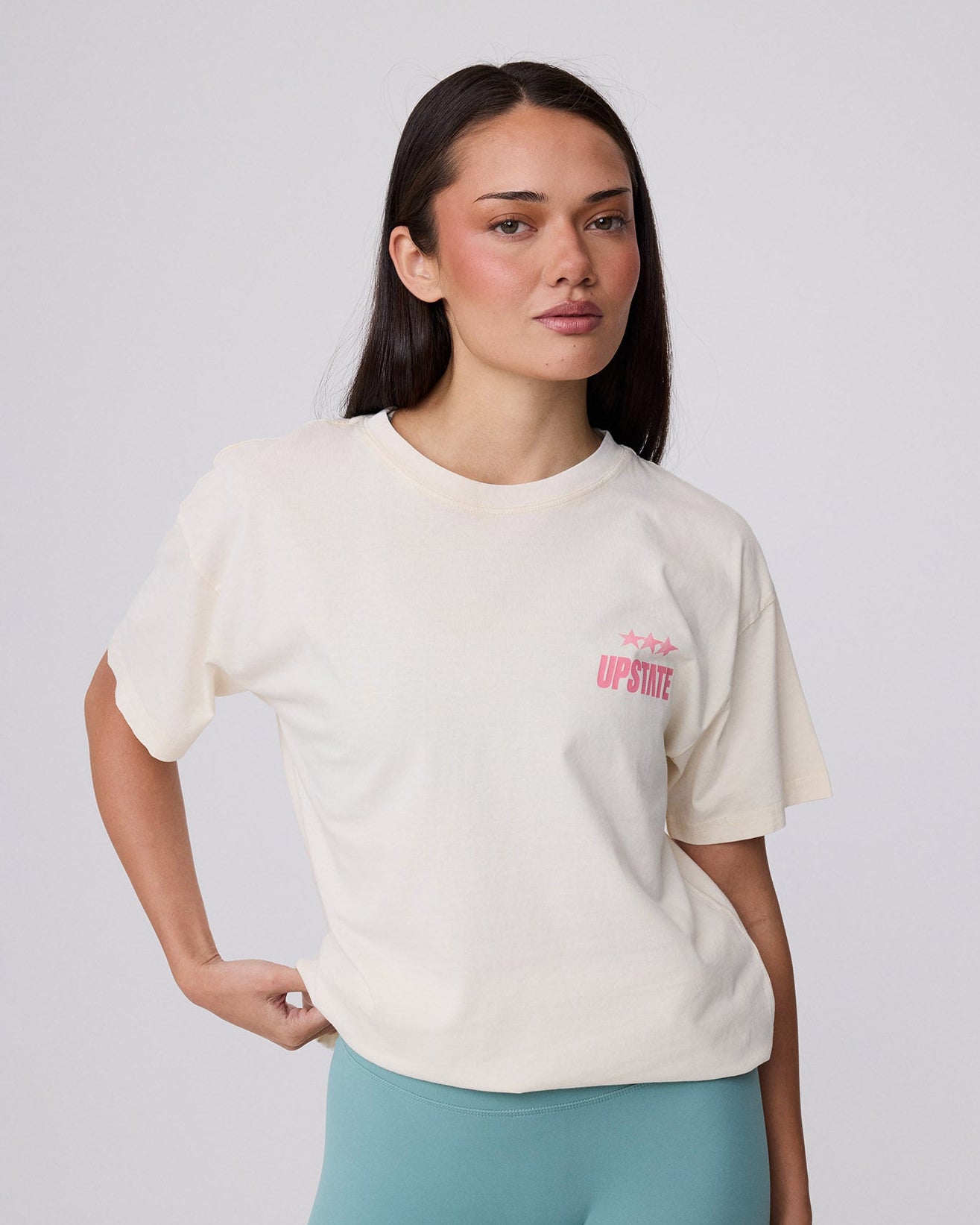 Woman wearing a white t-shirt with text and light blue leggings on a plain background