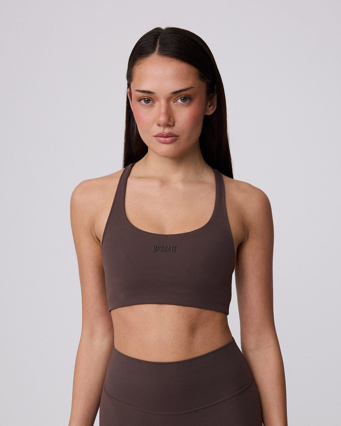 Woman wearing a brown sports bra and leggings on a light gray background
