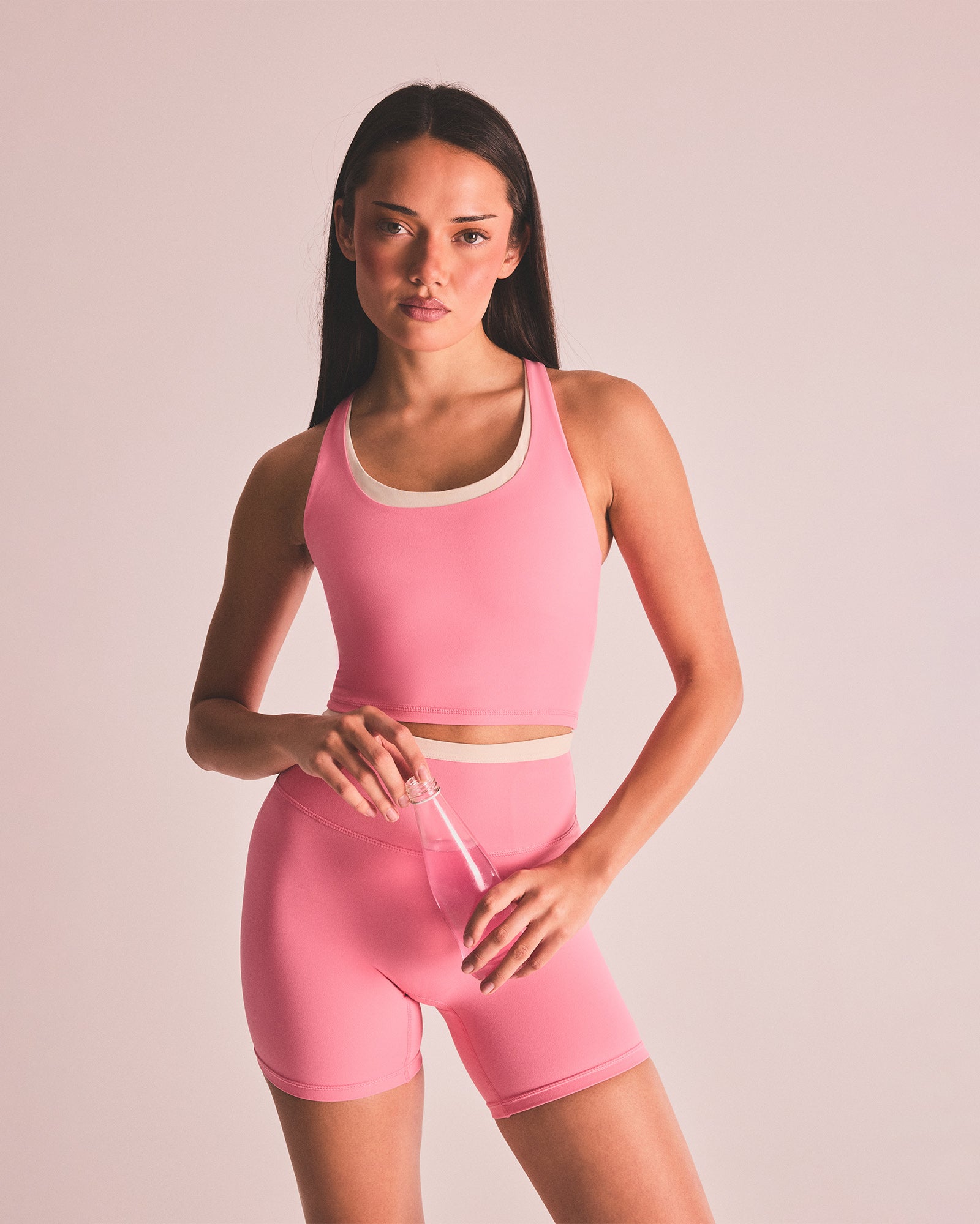 Woman wearing a pink athletic outfit holding a straw against a plain background
