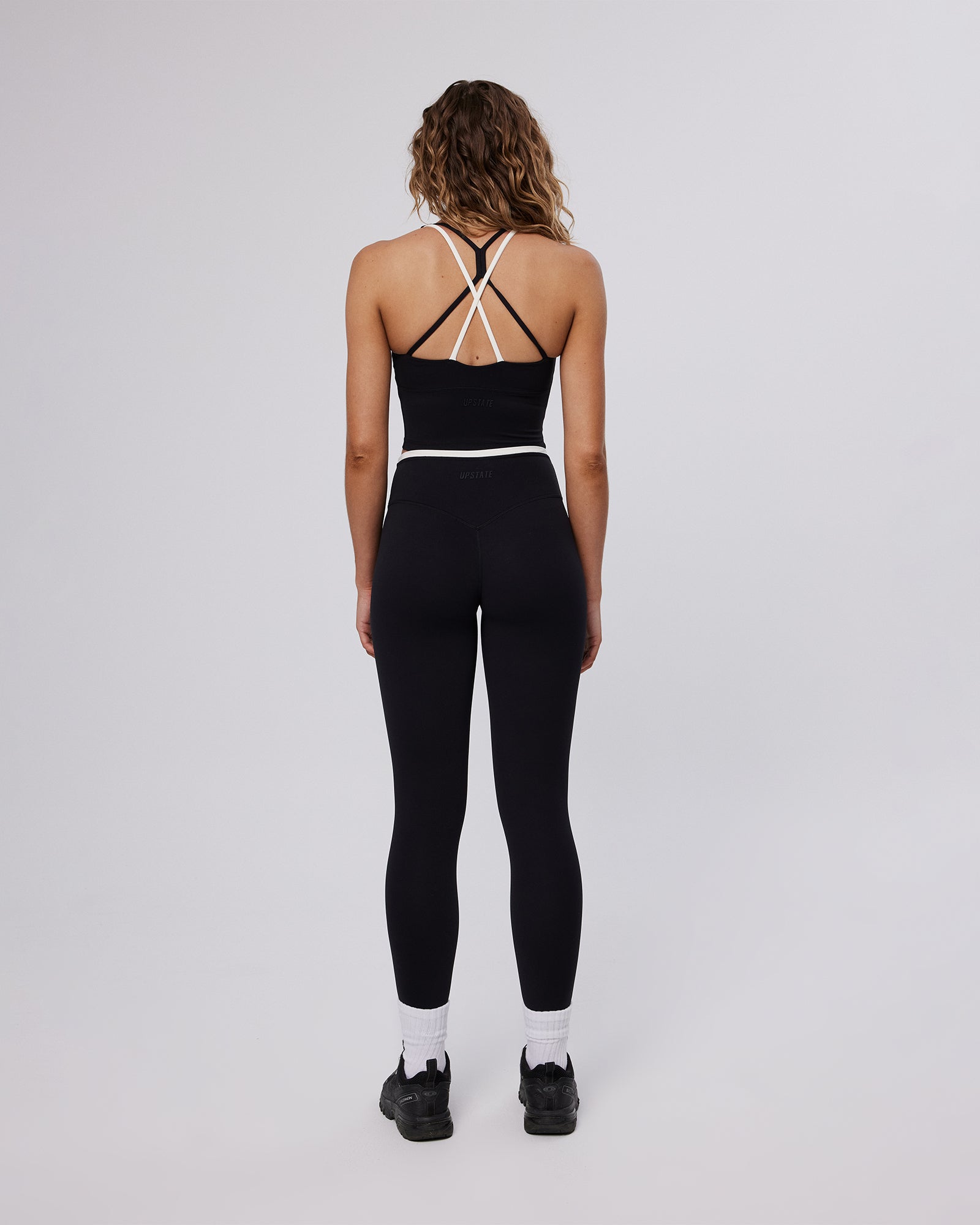 Person wearing a black athletic outfit with white socks on a light gray background