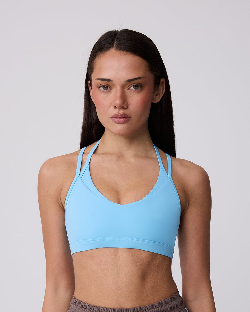 Woman wearing a blue sports bra and brown shorts on a plain background